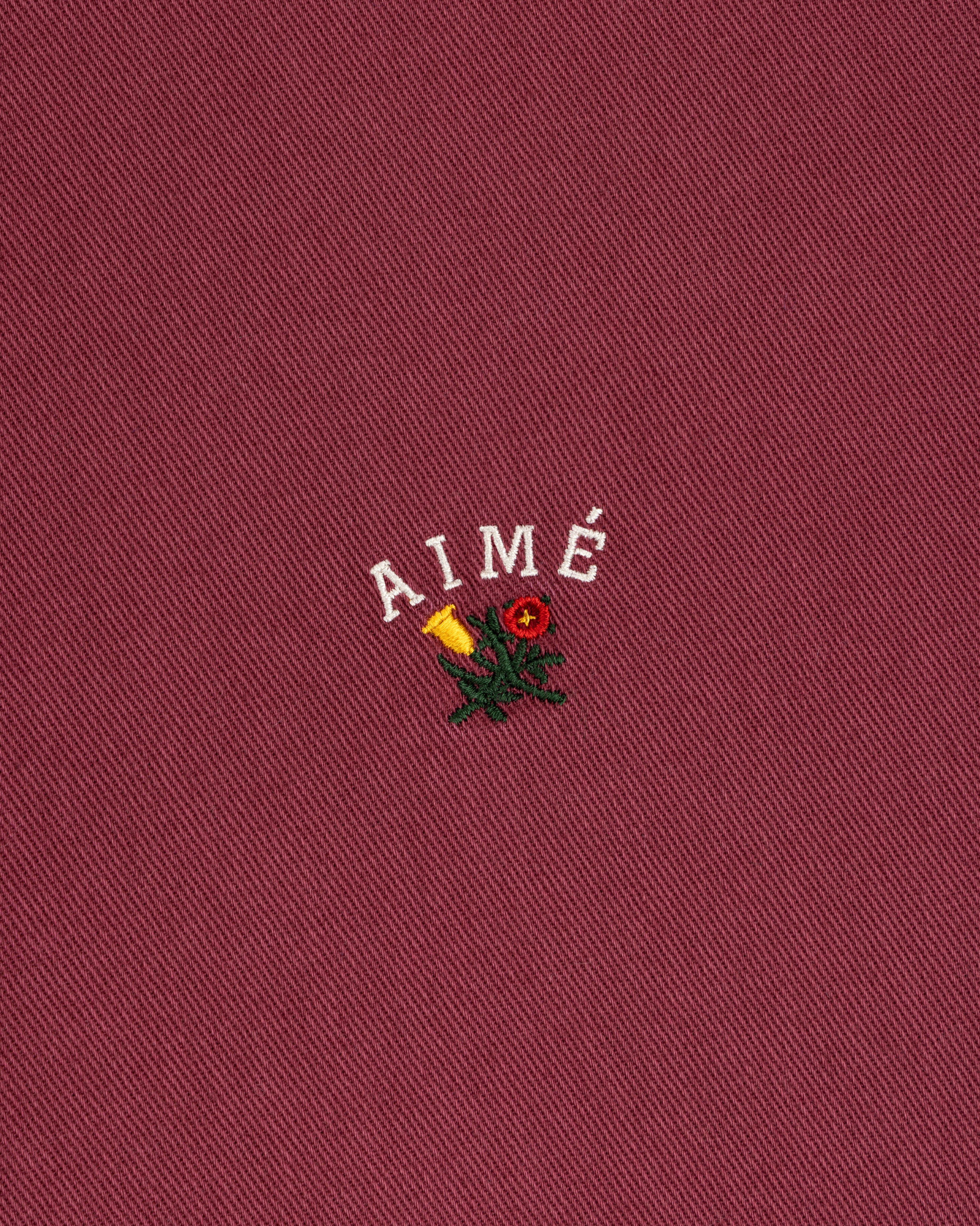 Garment Dyed Leon Overshirt in red with “AIMÉ” above an embroidered rose and candle.