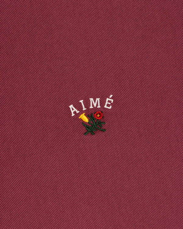 Garment Dyed Leon Overshirt in red with “AIMÉ” above an embroidered rose and candle.