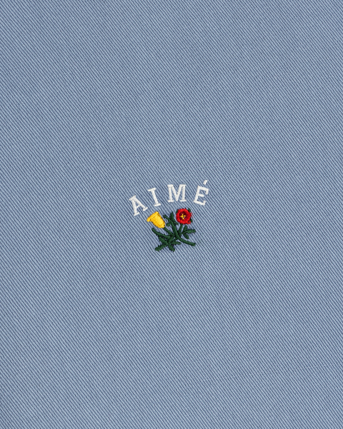 White AIMÉ embroidery and flower on blue textured fabric of the Garment Dyed Leon Overshirt.