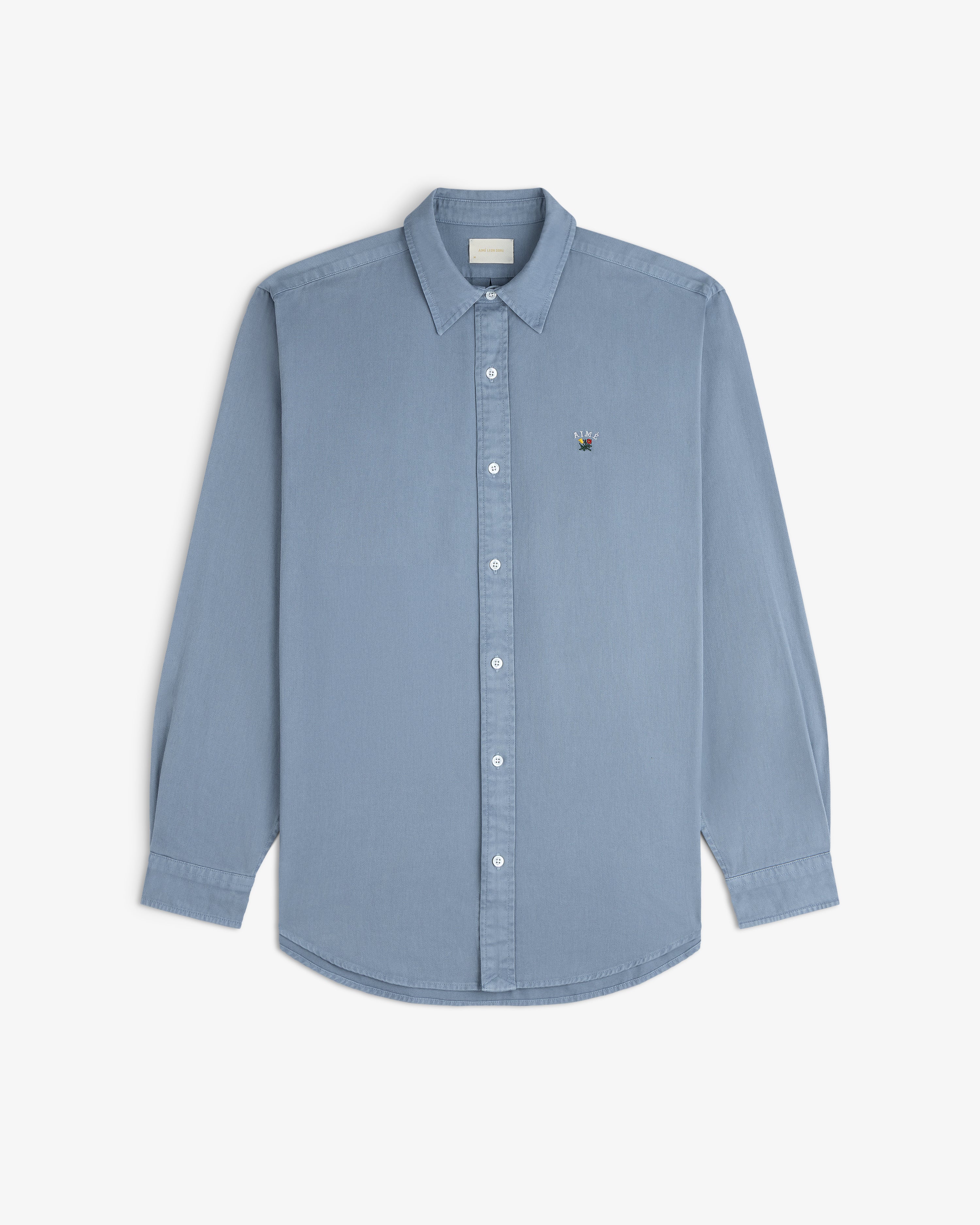 Garment Dyed Leon Overshirt in light blue with long sleeves and chest logo, shown on a white background.