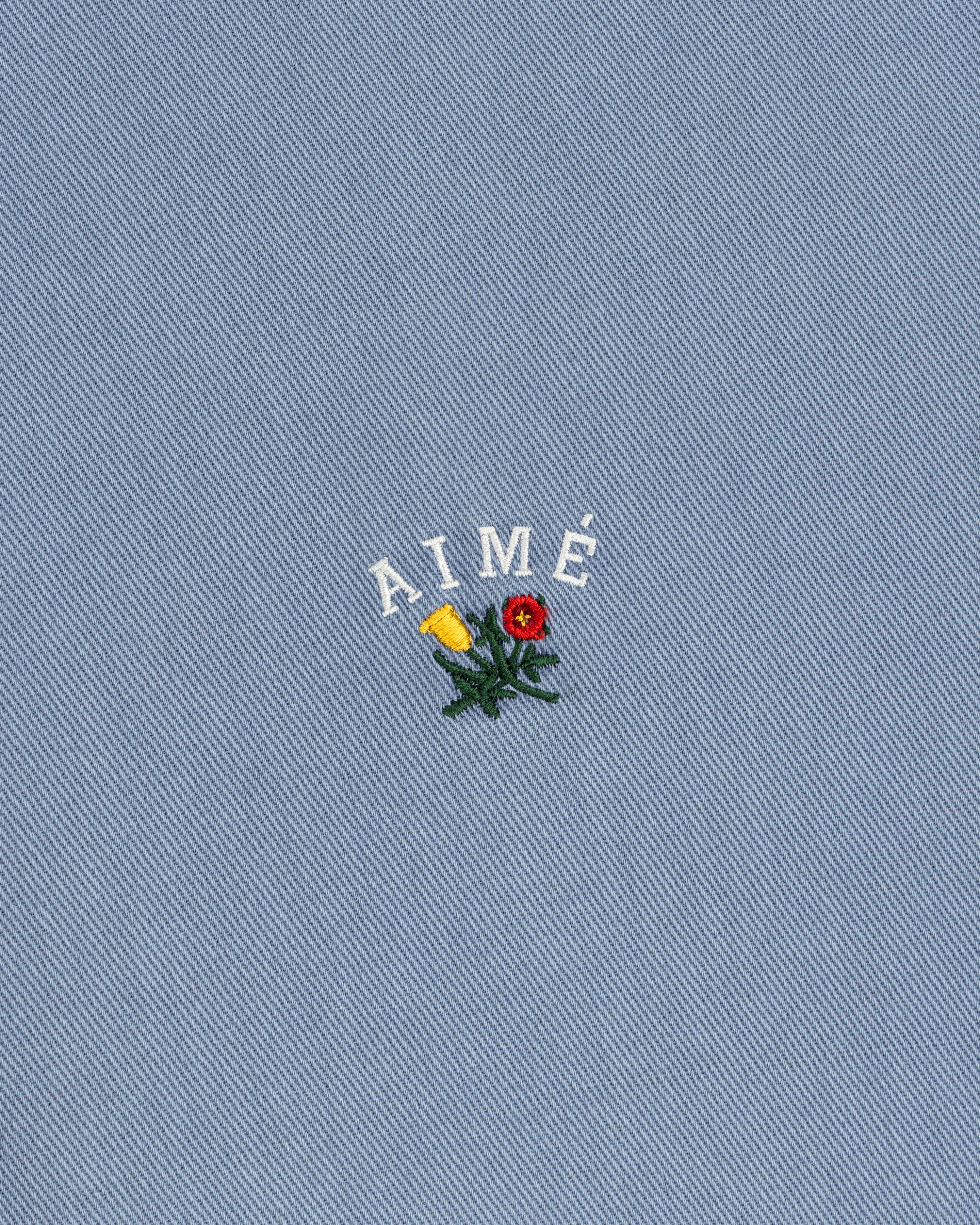 White AIMÉ embroidery and flower on blue textured fabric of the Garment Dyed Leon Overshirt.