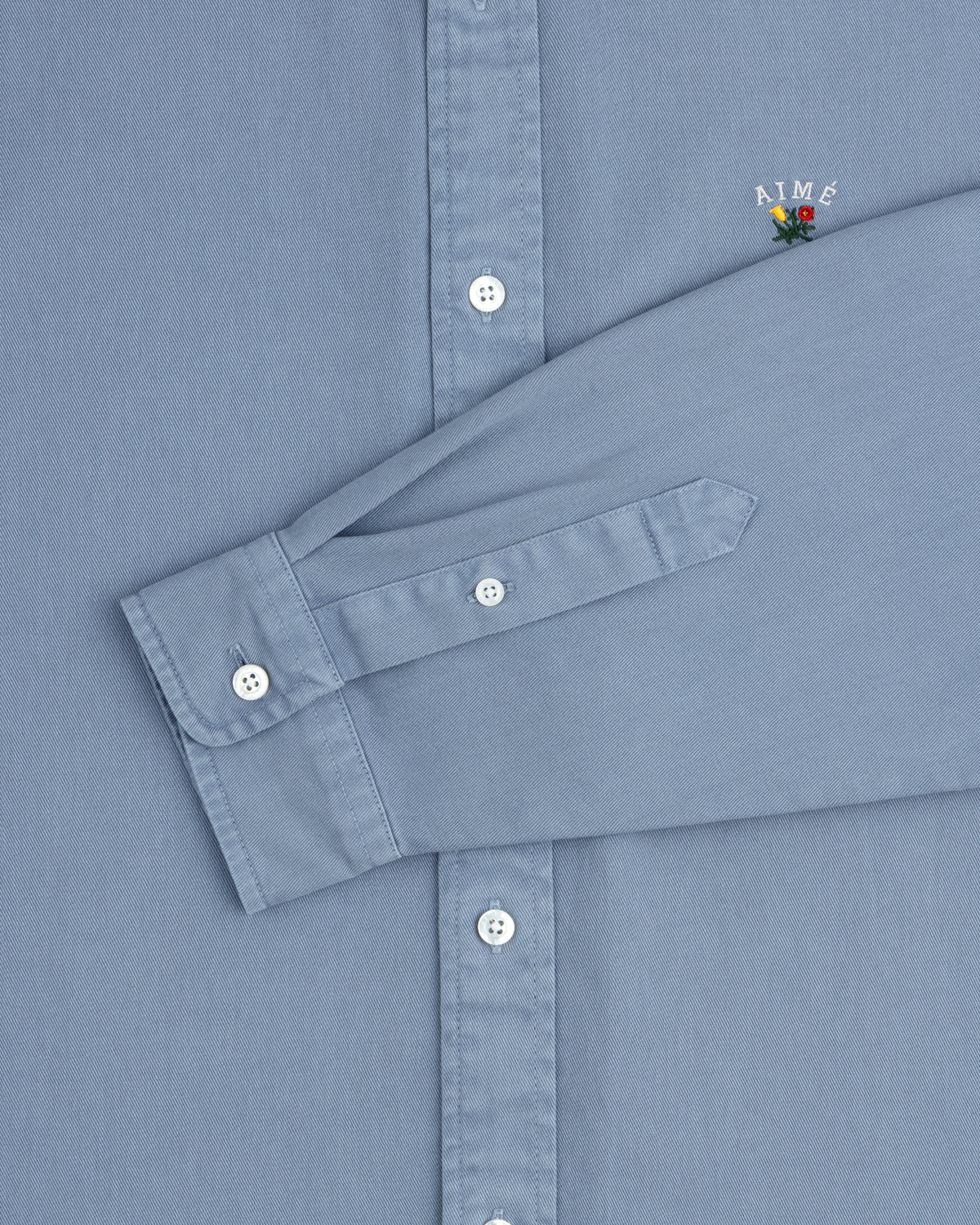 Garment Dyed Leon Overshirt: Light blue, white buttons, AIMÉ logo with flower on chest.