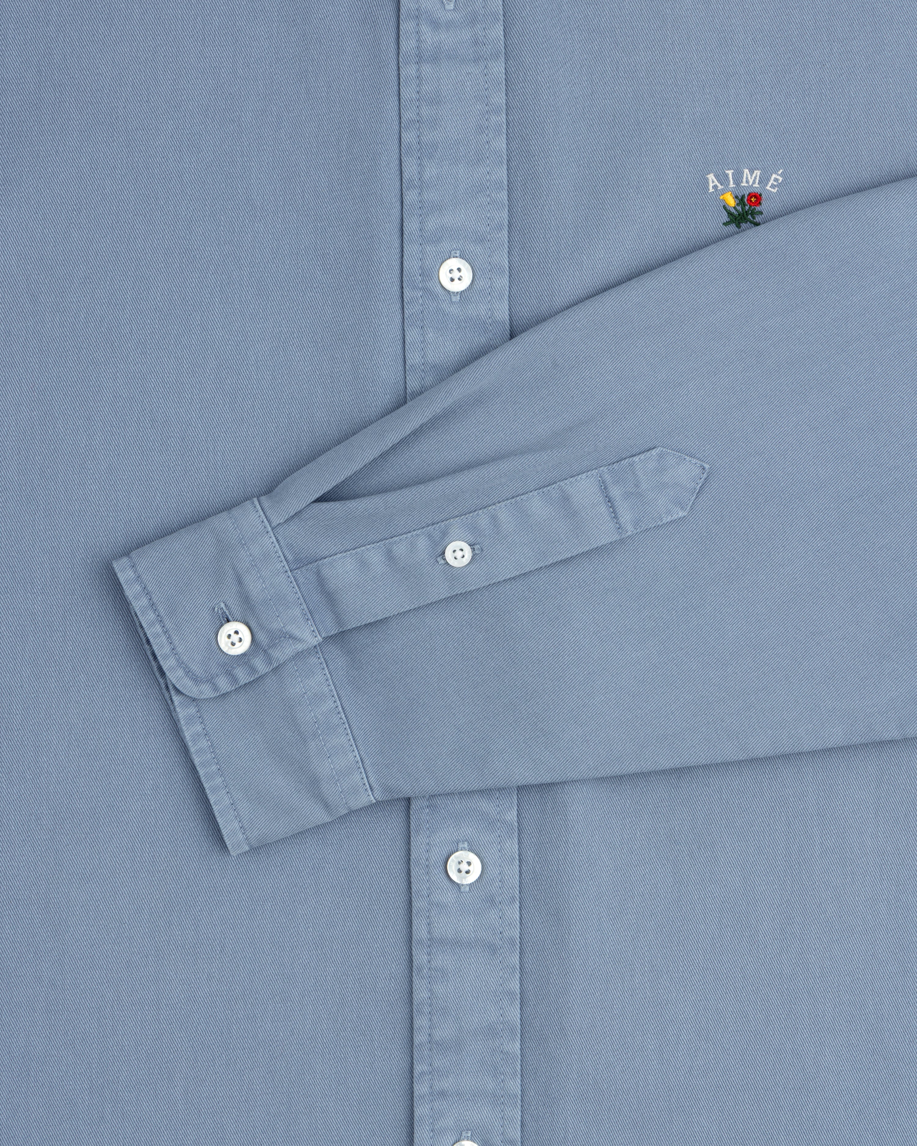 Garment Dyed Leon Overshirt: Light blue, white buttons, AIMÉ logo with flower on chest.
