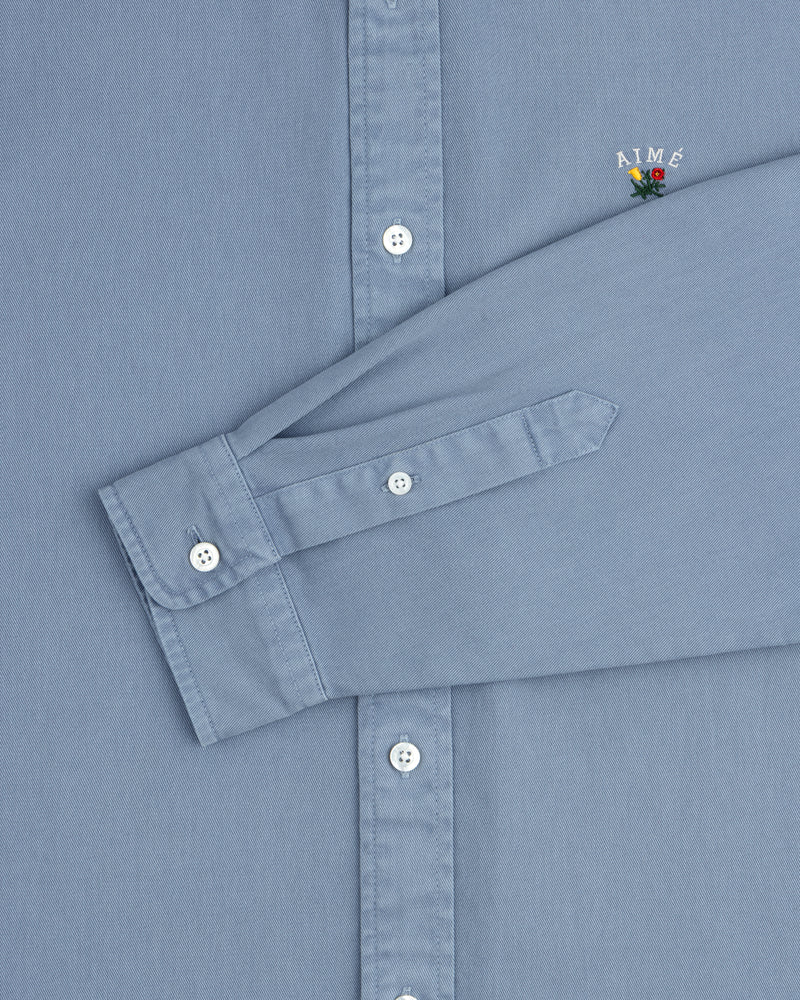 Garment Dyed Leon Overshirt: Light blue, white buttons, AIMÉ logo with flower on chest.