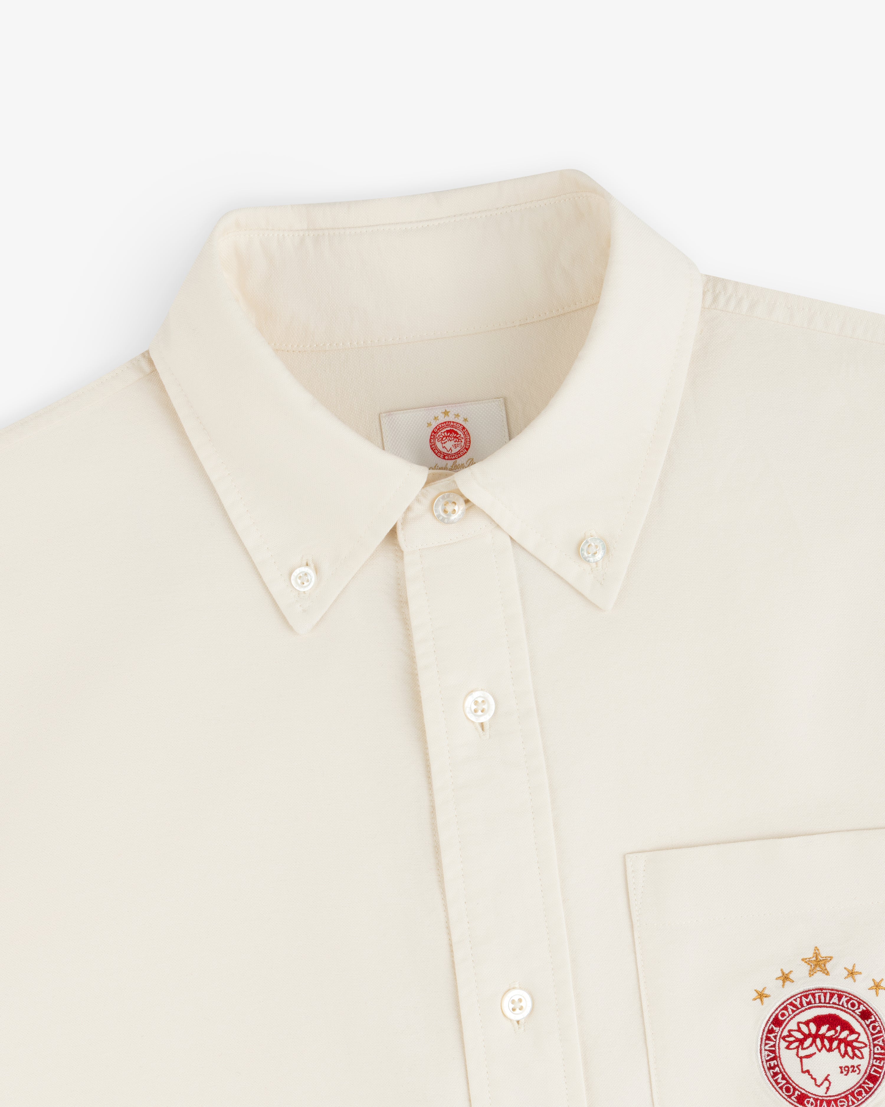 Cream-colored ALD / Olympiacos F.C. Logo Oxford Shirt with embroidered logos on the chest pocket and inner neck label.