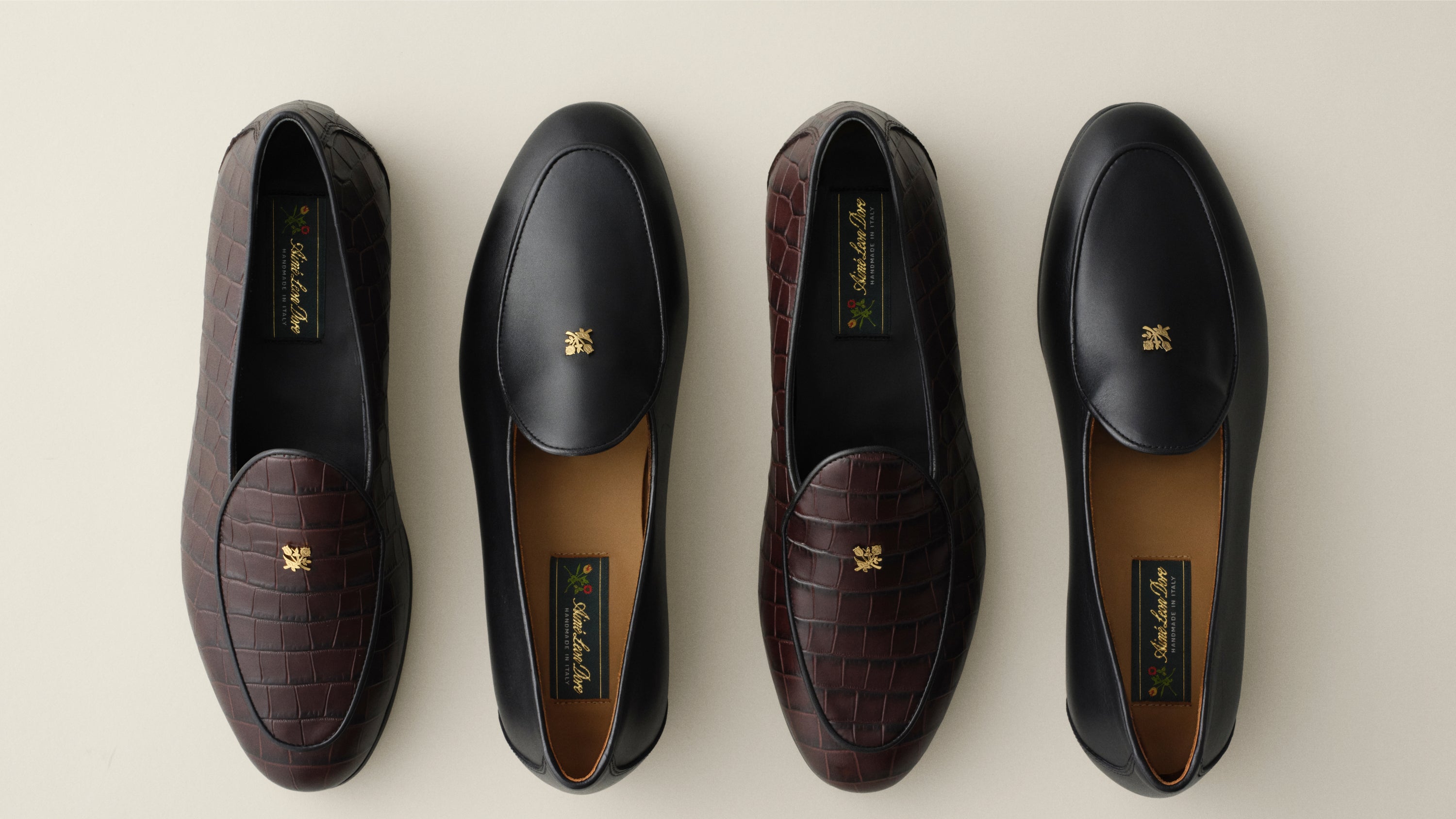Four luxury loafers in black leather and dark brown croc-embossed leather, with gold-tone logo hardware on the vamp and a tan interior lining.
