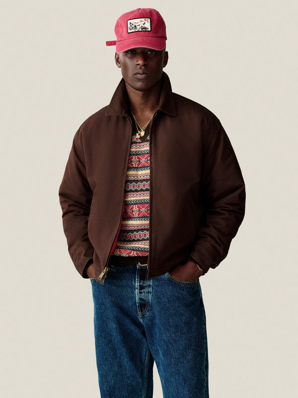 Person in a Fair Isle V-Neck Sweater, blue jeans, and red cap stands with hands in pockets against a plain background.