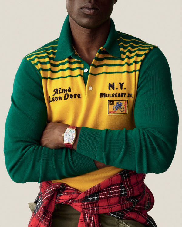 Man in Merino Wool Knit Cycling Polo by Aimé Leon Dore, green/yellow, N.Y. Mulberry St. text, arms crossed.
