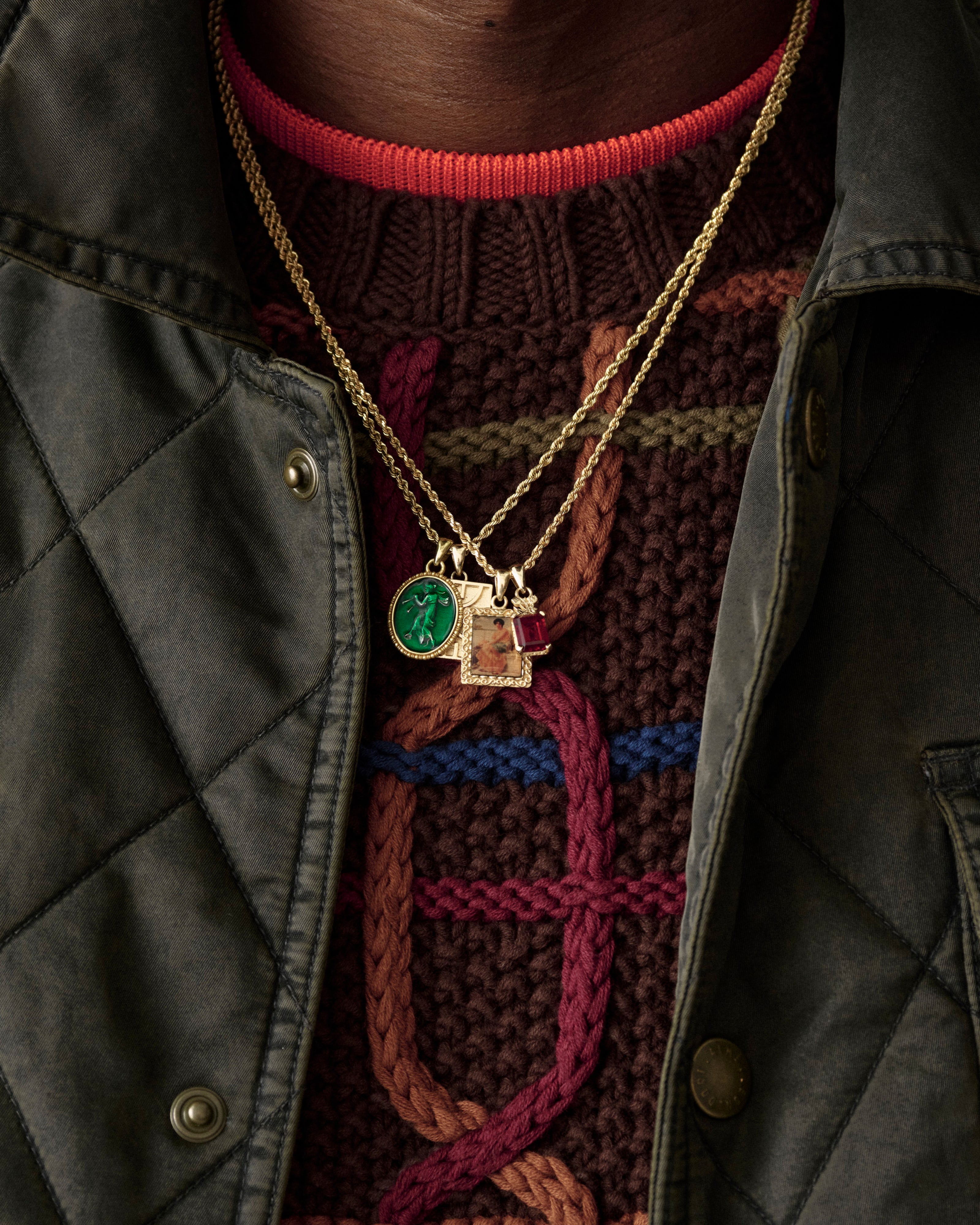 A close-up of the 14Kt Gold Crest Gemstone Pendant worn over a textured sweater and green quilted jacket.