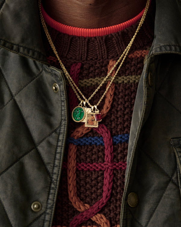 A close-up of the 14Kt Gold Crest Gemstone Pendant worn over a textured sweater and green quilted jacket.