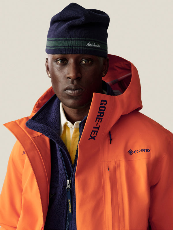 Man wearing a Stripe Knit Beanie, orange GORE-TEX jacket, blue fleece, and yellow shirt, looking at the camera.