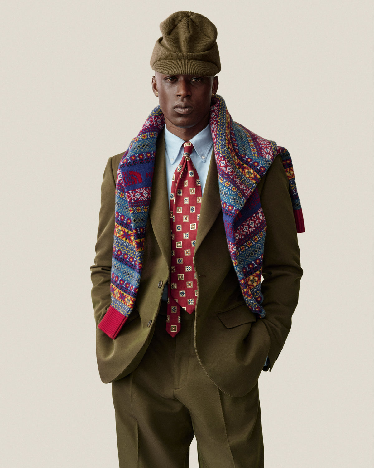 A man in an olive Wool Blend Suit Trouser, blue shirt, red tie, knit beanie, and colorful scarf.