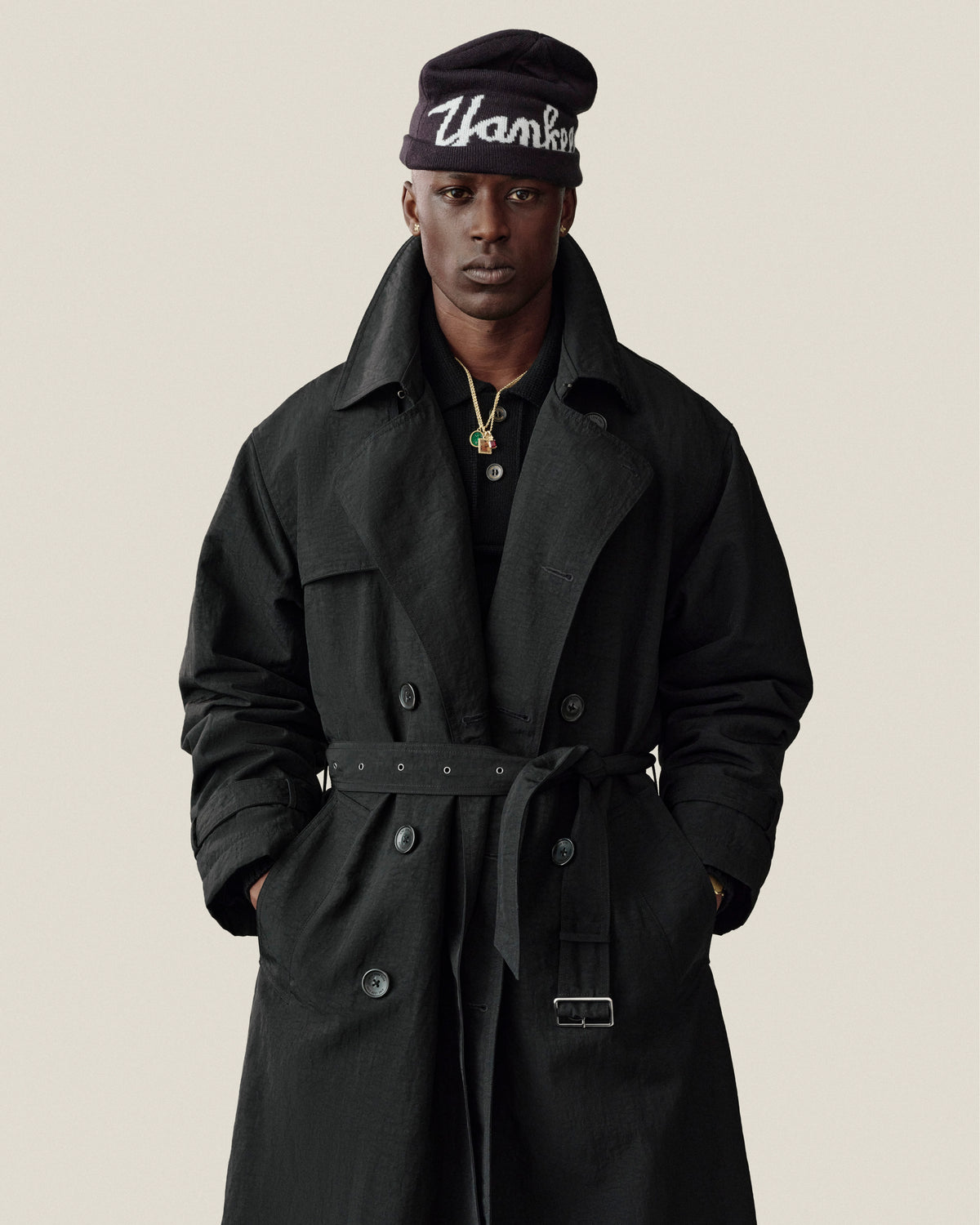 Man wears Double Breasted Nylon Trench Coat and beanie, “Thank You” text, hands in pockets, neutral background.