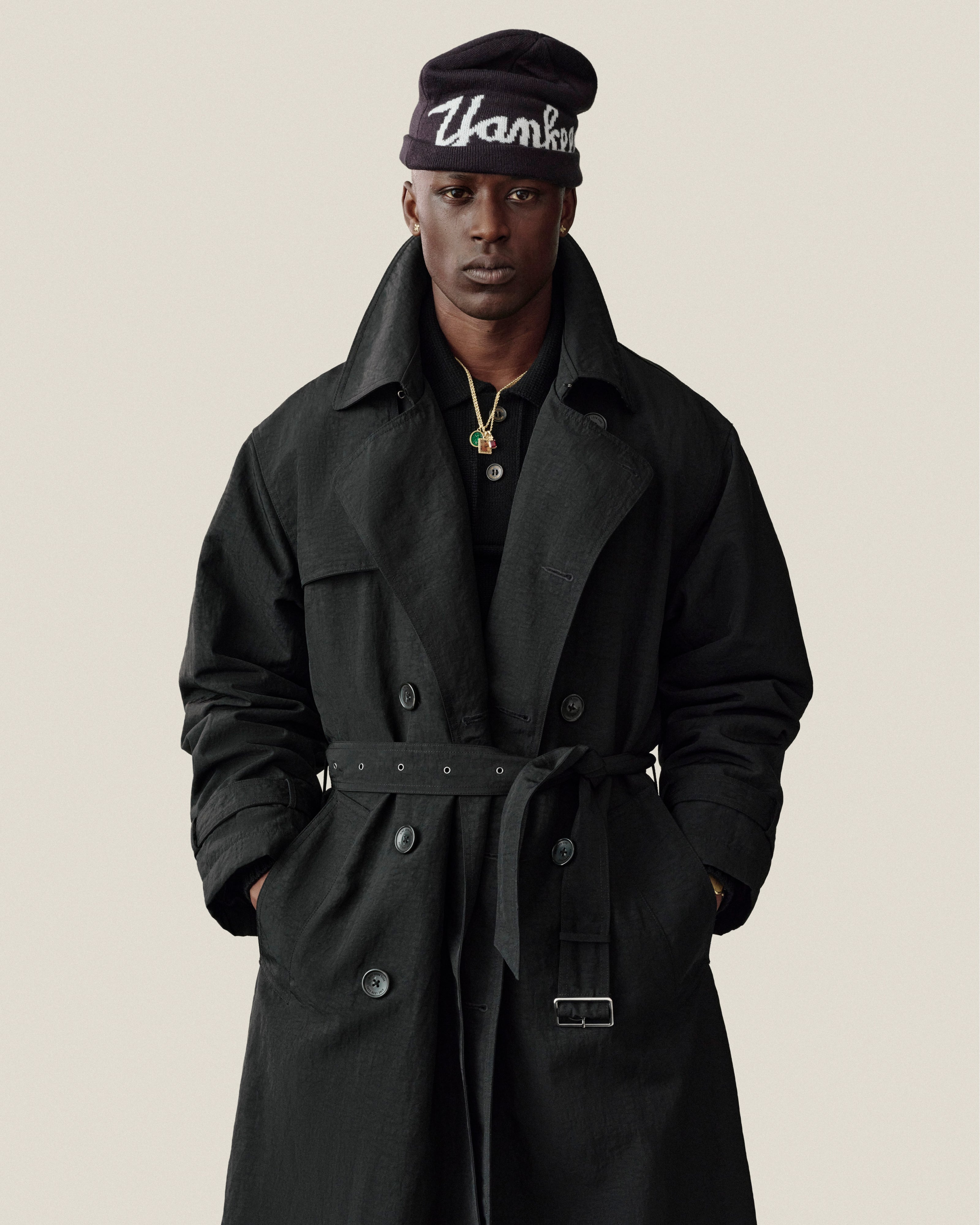 Man wears Double Breasted Nylon Trench Coat and beanie, “Thank You” text, hands in pockets, neutral background.