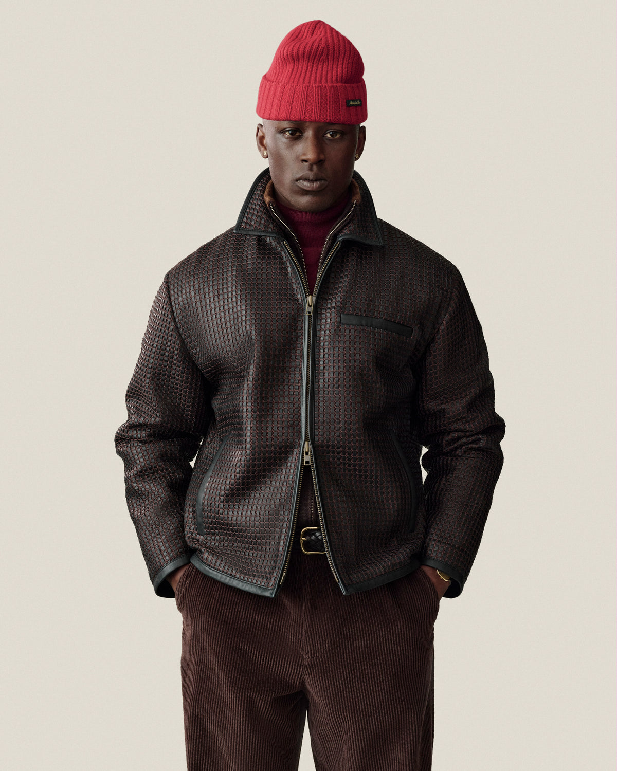 A man wearing a dark brown Woven Leather jacket, a red knit beanie, and dark trousers.