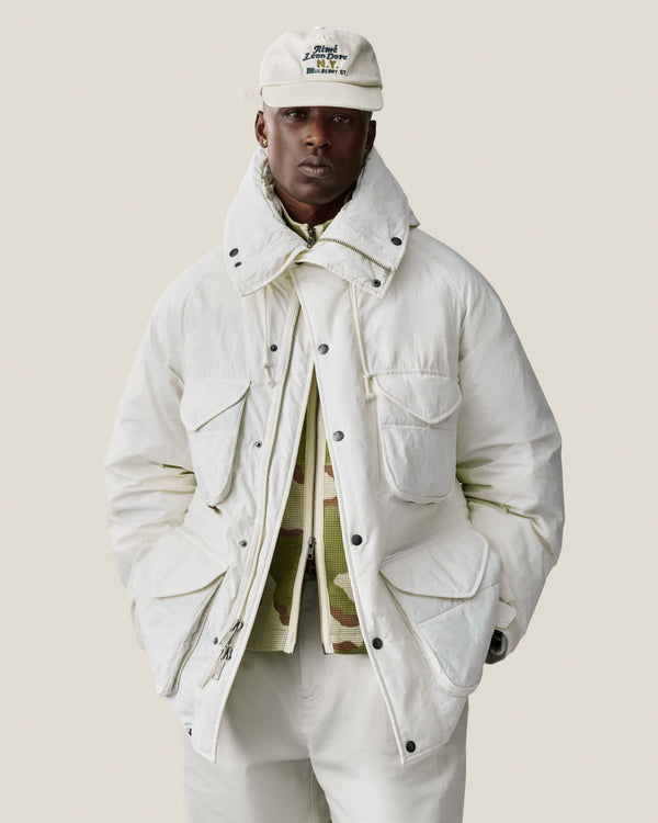 Man wearing a Mulberry Chainstitch Hat, white puffer jacket, and pants against a plain light background.