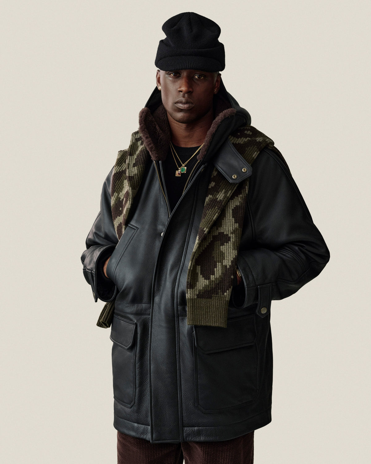 A person wearing a black Wool Brim Beanie, a leather jacket with a faux-fur lining, and a camouflage scarf.