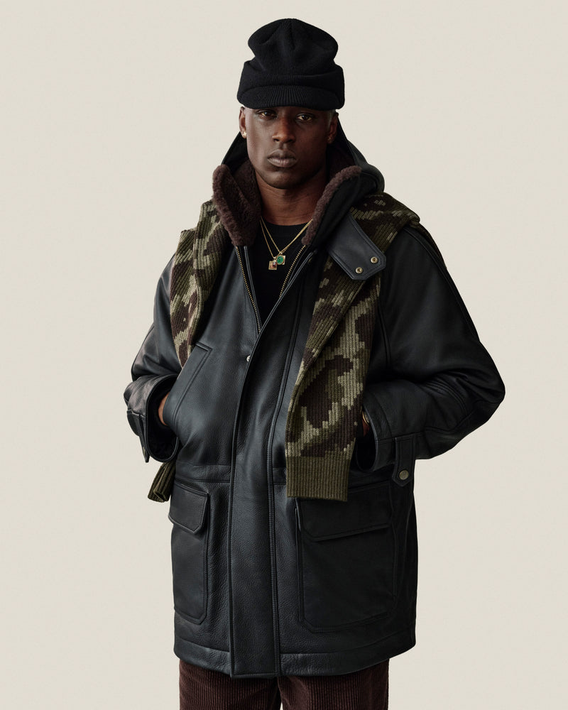 A person wearing a black Wool Brim Beanie, a leather jacket with a faux-fur lining, and a camouflage scarf.