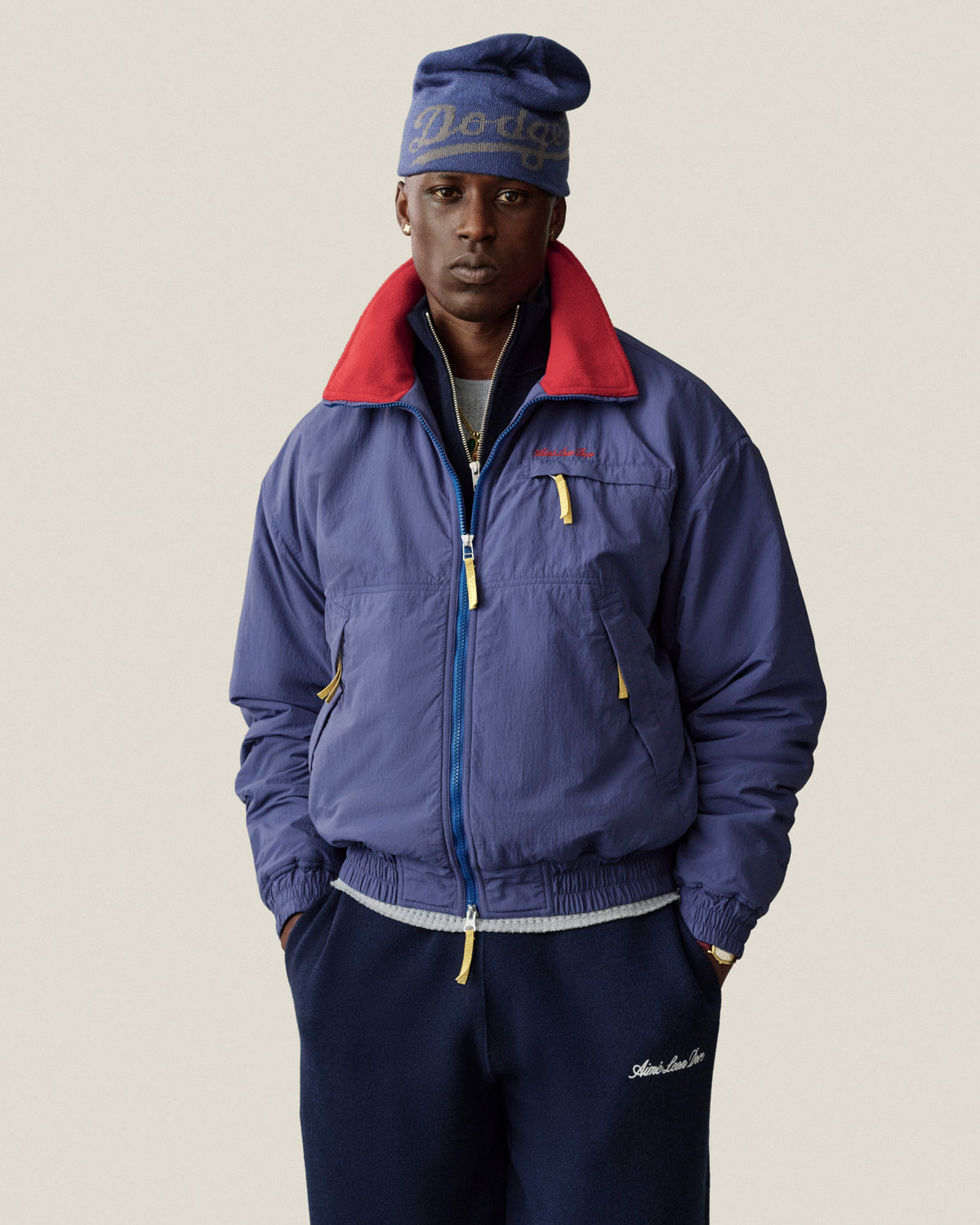 A man wearing an ALD / New Era Dodgers Beanie and a blue zip-up jacket with a red collar.
