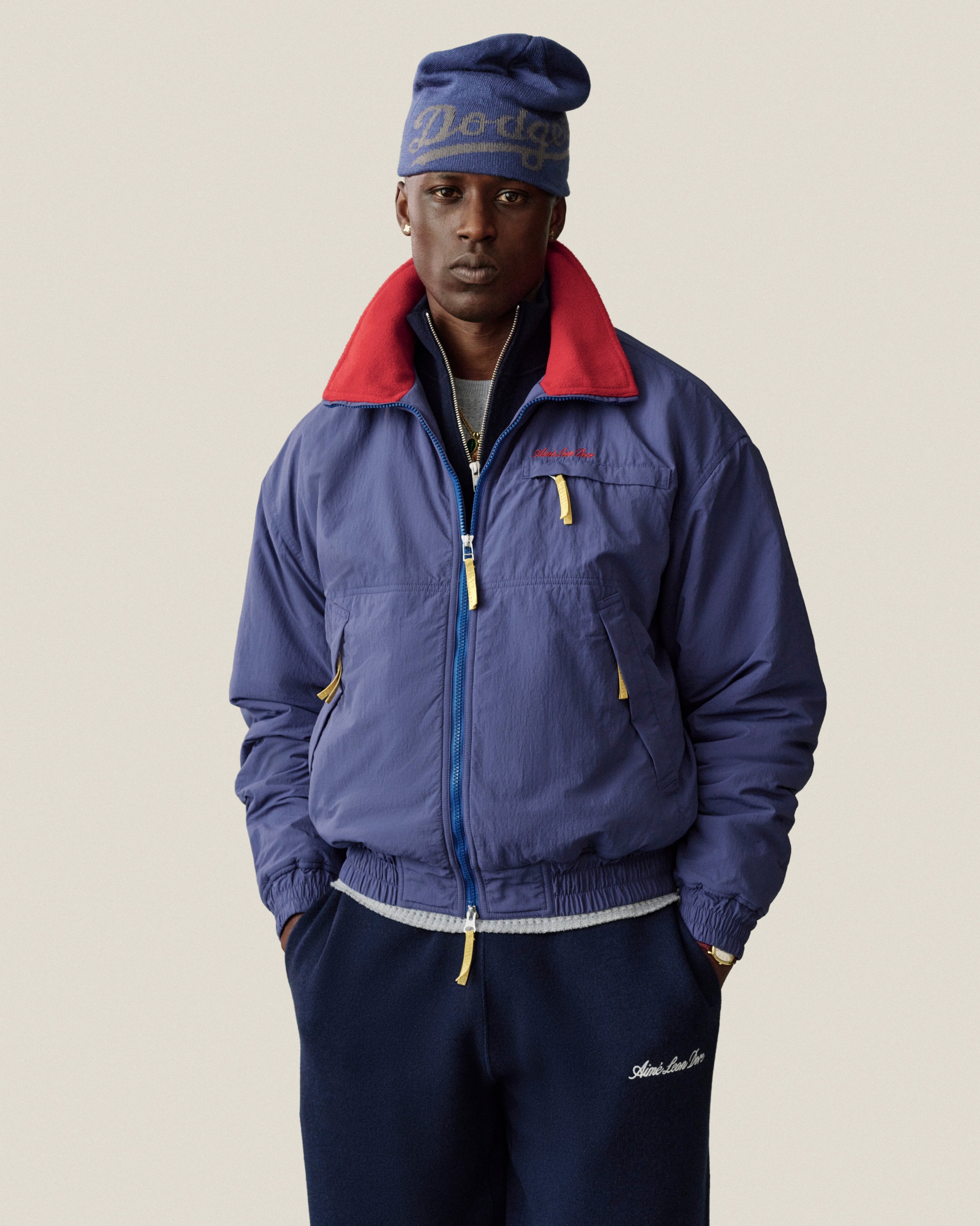 A man wearing an ALD / New Era Dodgers Beanie and a blue zip-up jacket with a red collar.