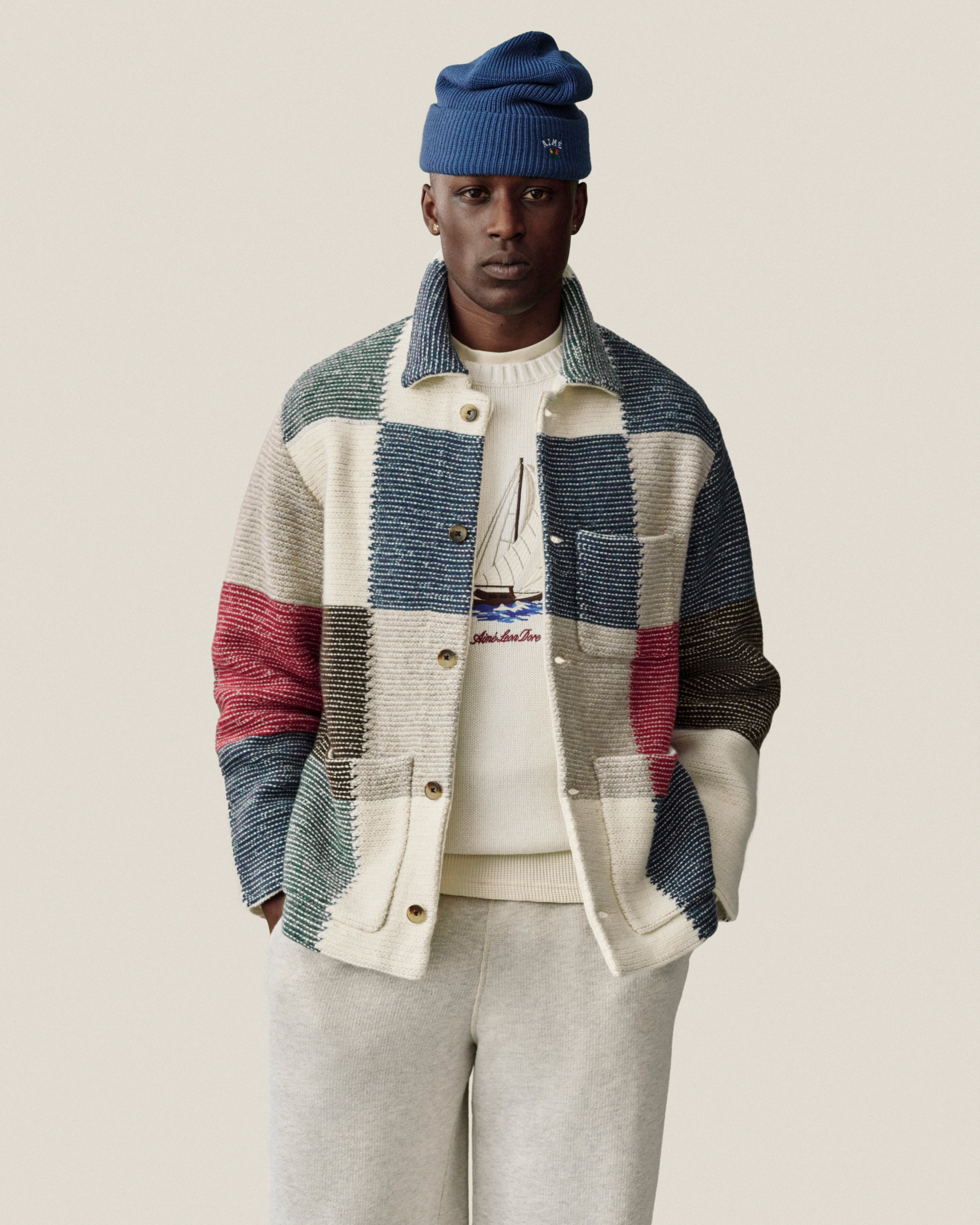 Man in blue beanie, patchwork jacket, sailboat sweater, and Stone Washed Marina Sweatpants with hands in pockets.