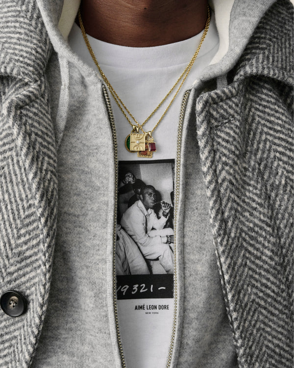 A person wears a 14Kt Gold Diamond Court Pendant, a graphic tee, and a gray herringbone coat with zipper and button.