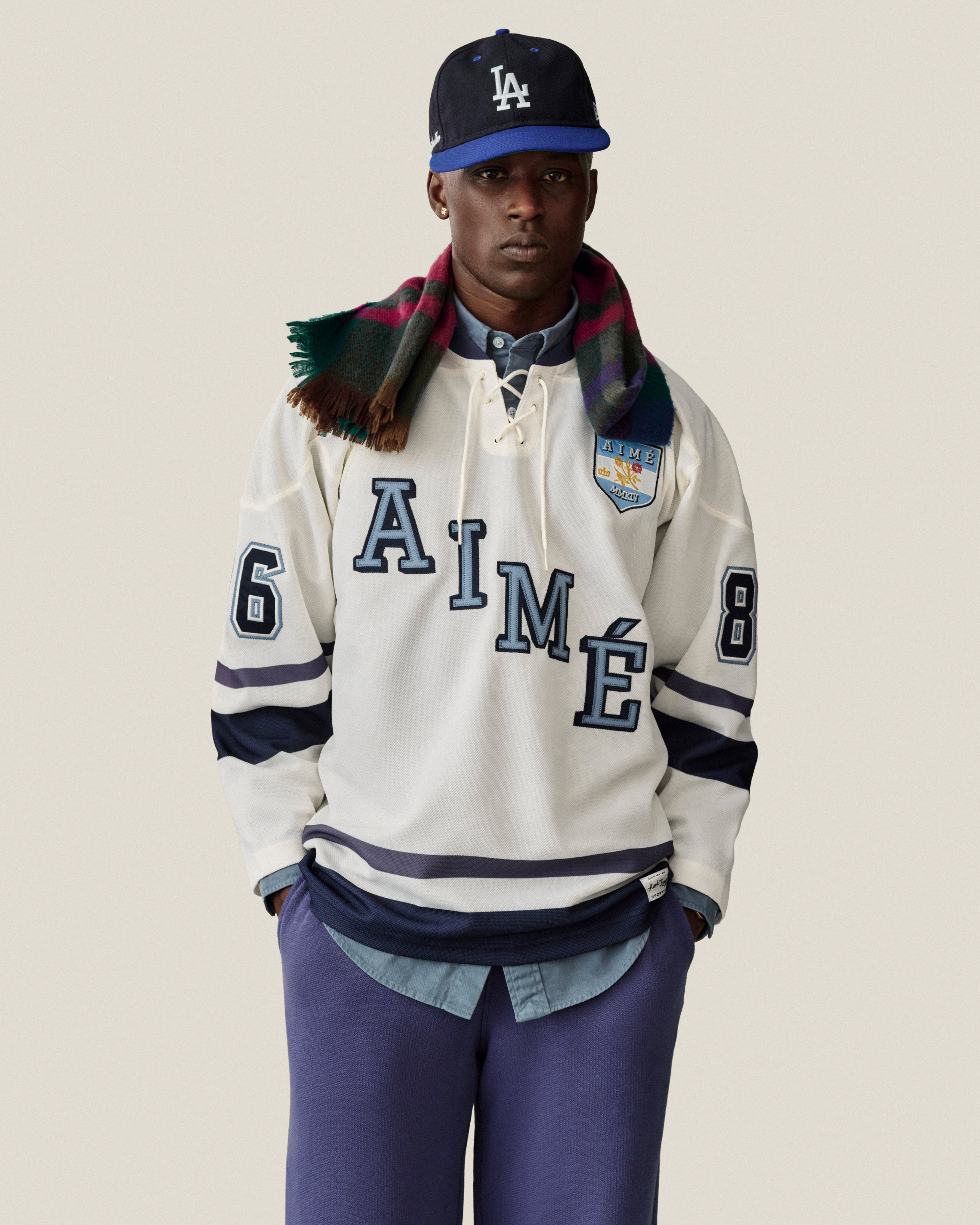 A person wearing a white lace-up Team Aimé Hockey Jersey with the text AIMÉ and the number 8 on the chest.