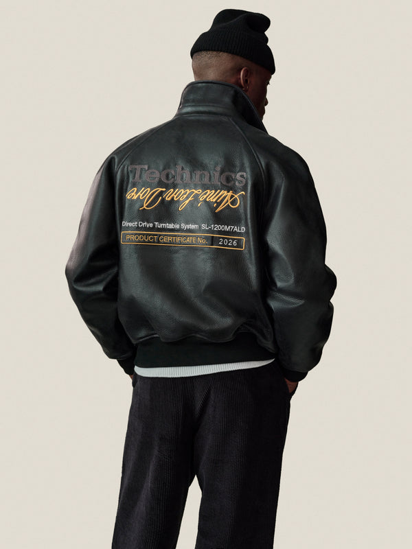 A person in a black beanie and the ALD / Technics Varsity Leather Jacket faces away against a plain background.