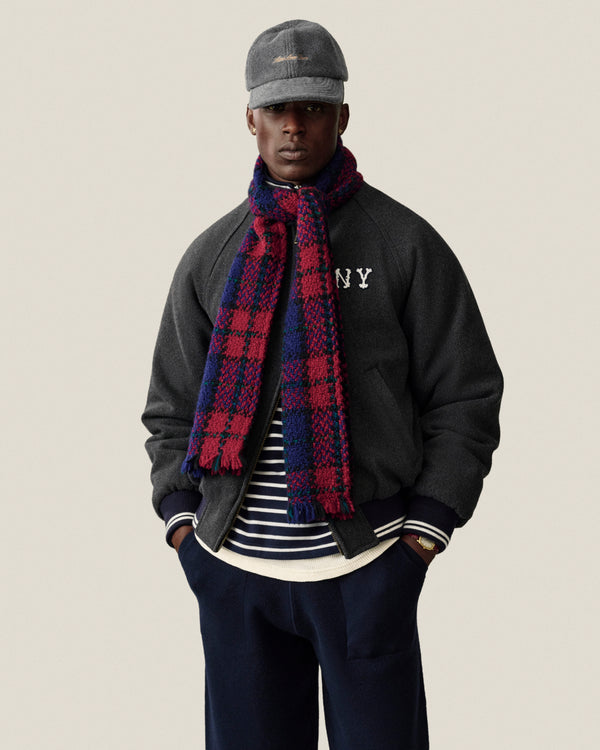 A man wears a gray NY jacket, Striped Crest Quarter Zip, blue pants, matching gray cap, and red-and-blue plaid scarf.