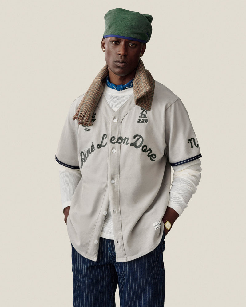 Man in a Mulberry Chainstitch Baseball Jersey, green beret, plaid scarf, white shirt, and blue striped pants.