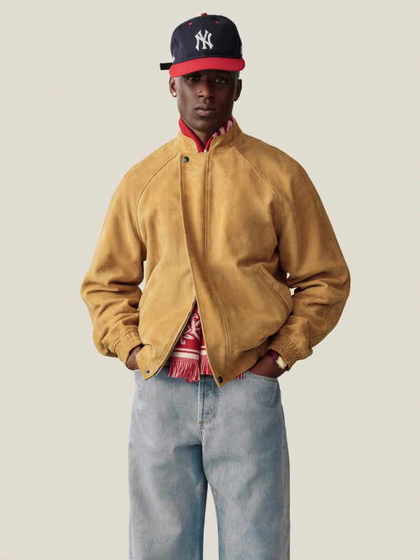 A man in a Suede Cafe Racer Jacket, red shirt, and light jeans wears a navy Yankees cap; neutral background.