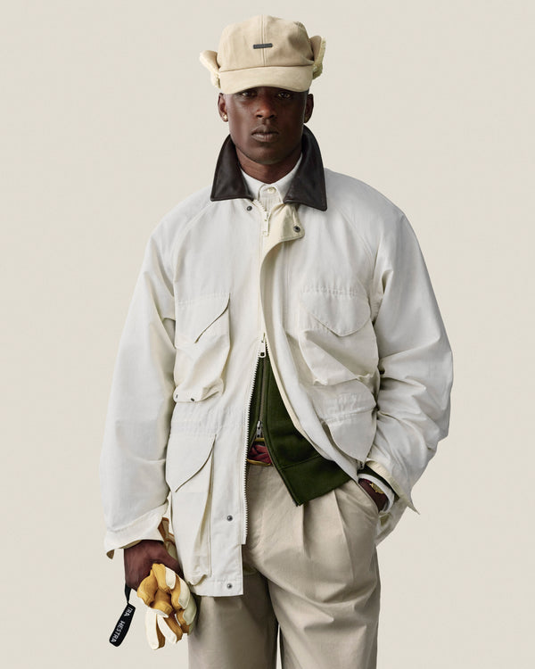 Man in Lightweight Barn Jacket and beige cap holds yellow gloves against a plain light background.
