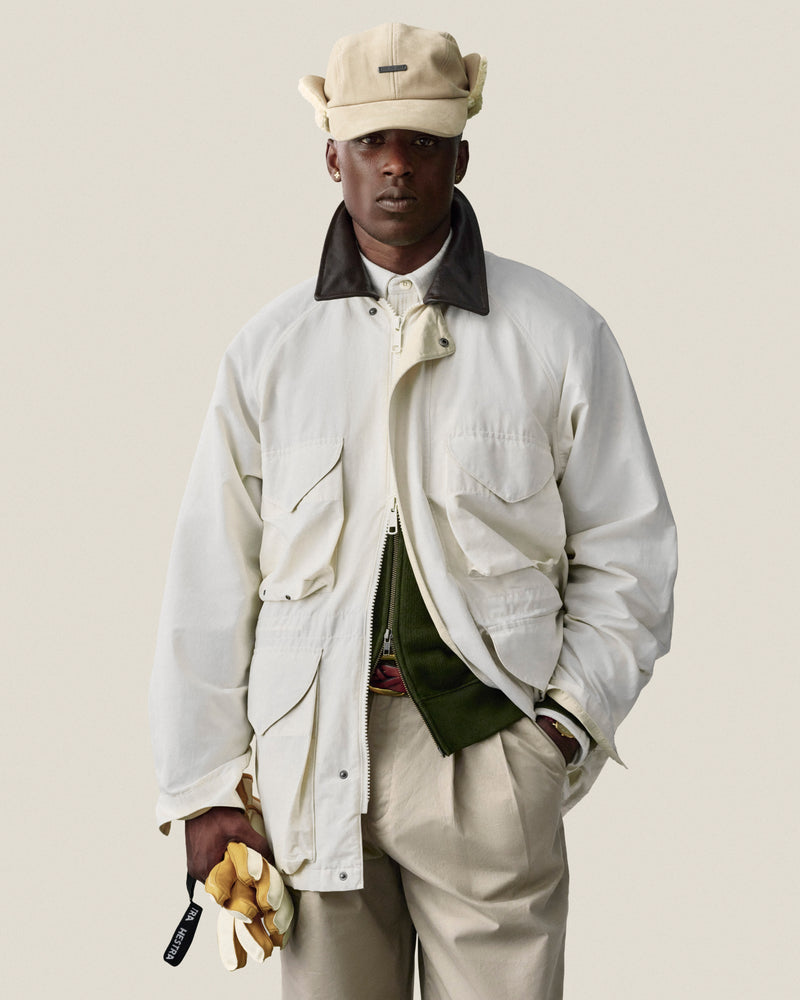 Man in Lightweight Barn Jacket and beige cap holds yellow gloves against a plain light background.