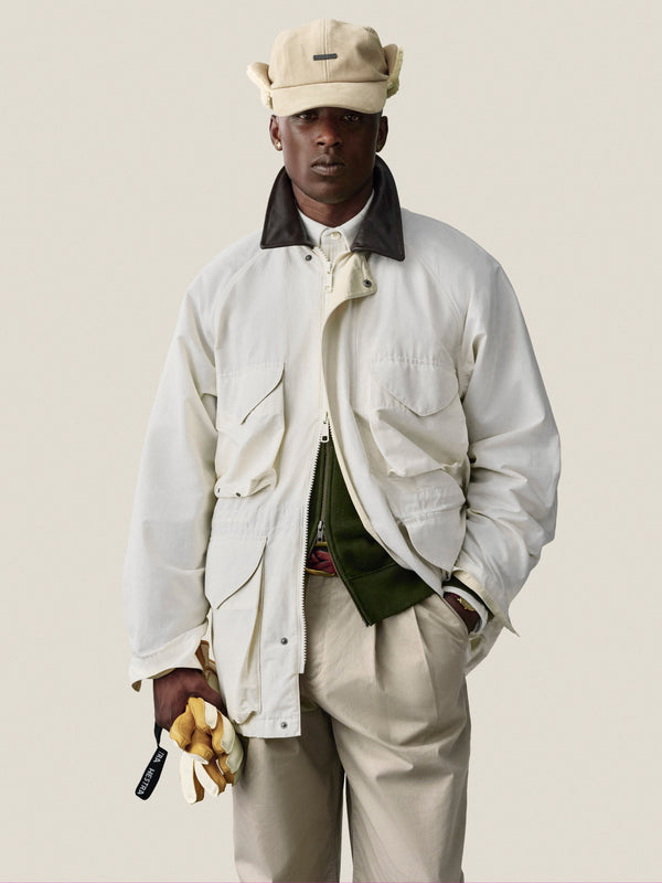 Man in Double Pleated Officer Pant, white jacket, and cap holds yellow gloves against a plain light background.
