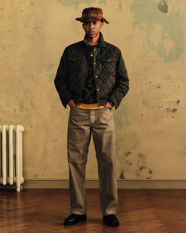 A man wearing a Quilted Trucker Jacket over a patterned sweater, yellow shirt, and a plaid bucket hat.