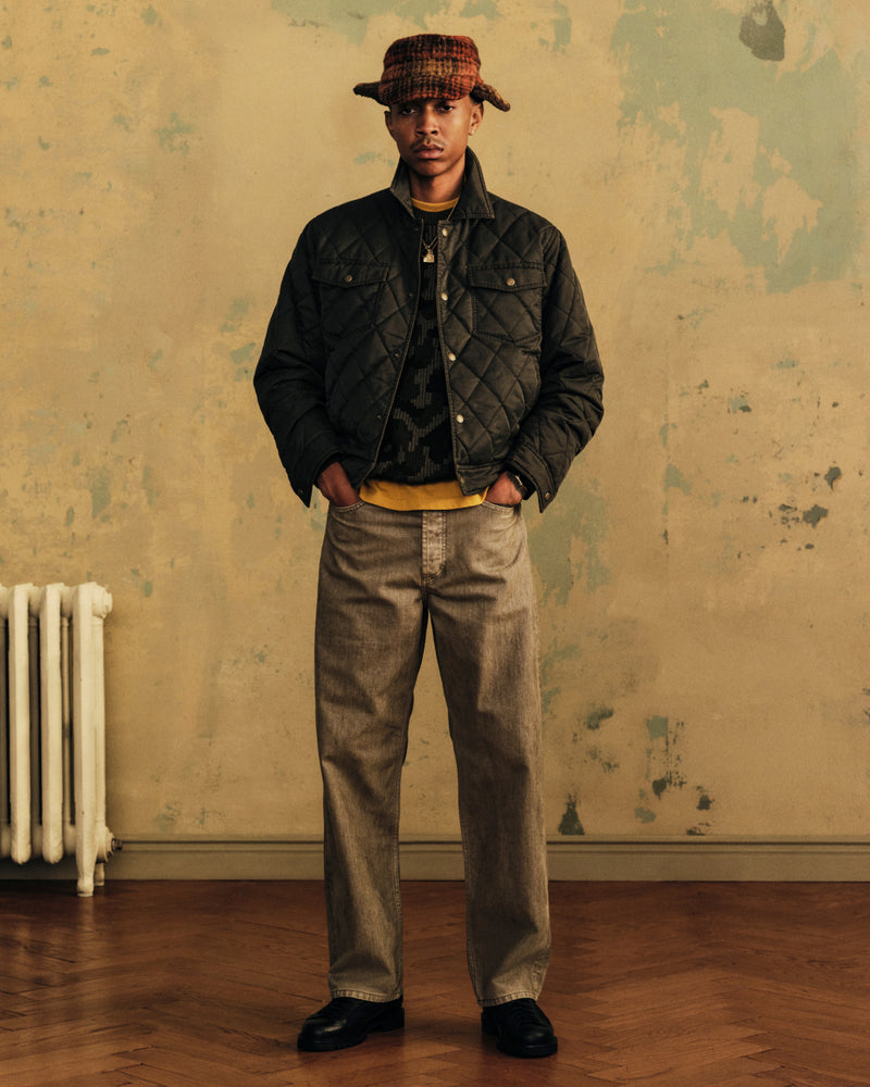 A man wearing a Quilted Trucker Jacket over a patterned sweater, yellow shirt, and a plaid bucket hat.