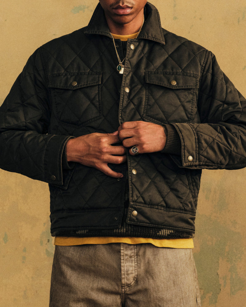 Person wearing a dark, diamond-quilted Quilted Trucker Jacket with buttoned chest pockets.