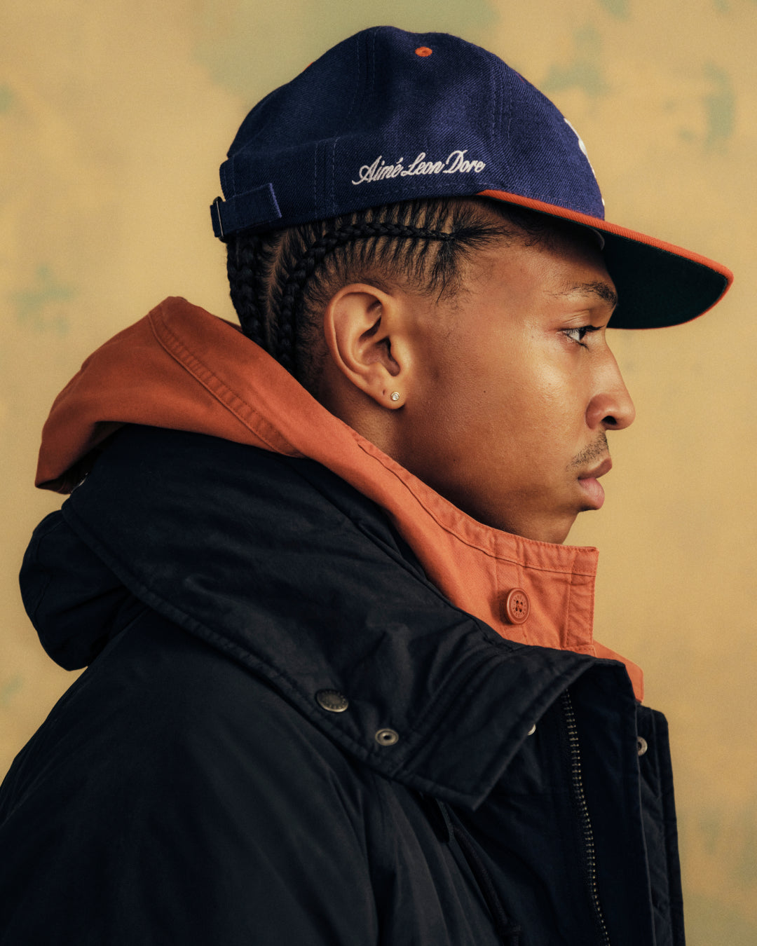Profile view of a person wearing an ALD / New Era Mets Retro Fit Hat in blue with an orange brim and script embroidery.