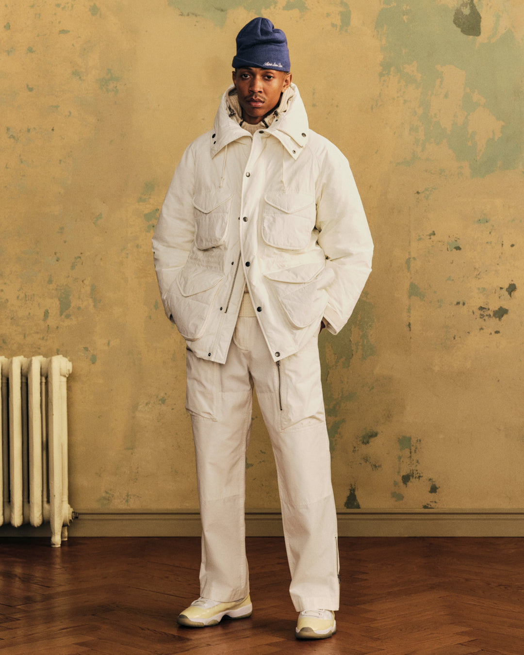A person wearing a white Down-Filled Surplus Parka with four pockets, matching pants, and a blue beanie.