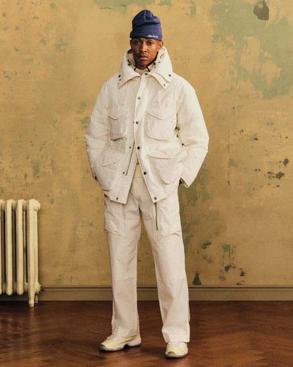 A person wearing a white Down-Filled Surplus Parka with four pockets, matching pants, and a blue beanie.