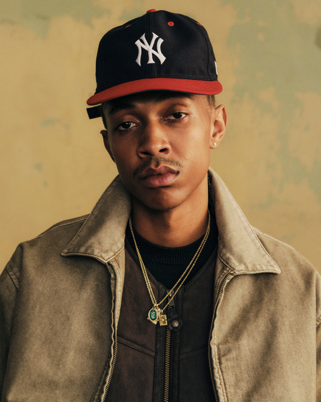 A man wears an ALD / New Era Yankees Retro Fit Hat, a navy blue baseball cap with a red brim and a white NY logo.
