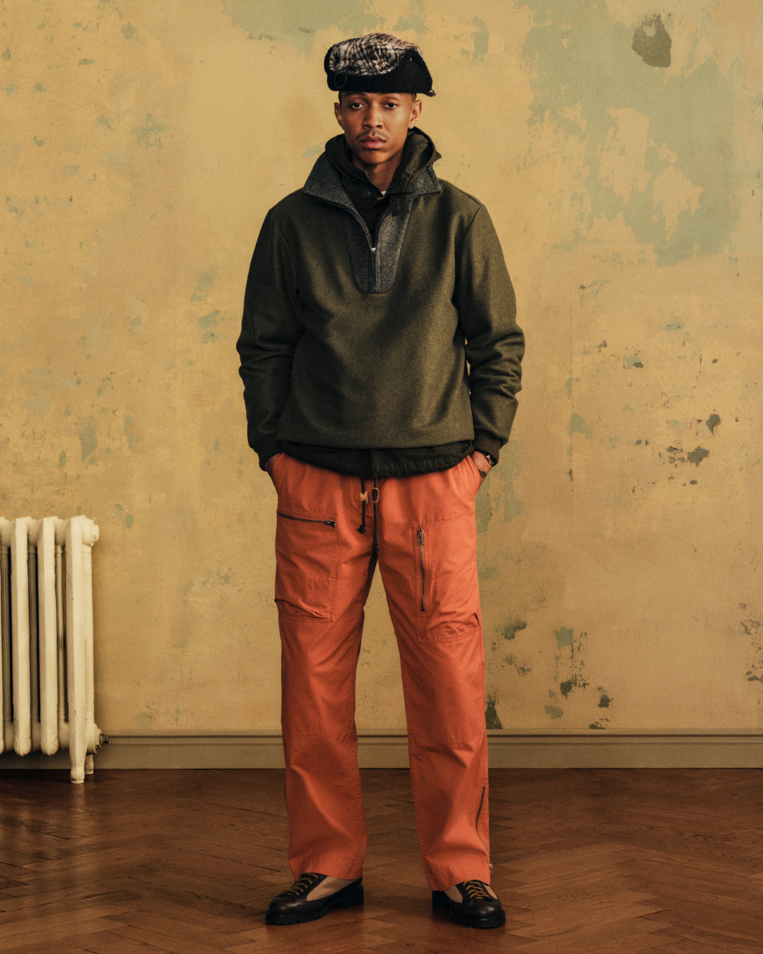 A man wears an olive green Surplus Fleece Quarter Zip Pullover and orange cargo pants.