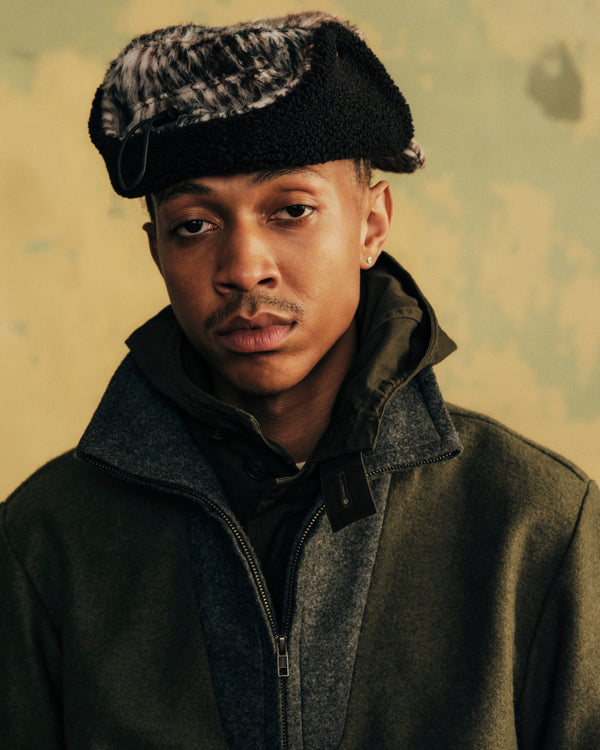 A person wears a Plaid Wool Hunting Hat with earflaps and an olive green coat.