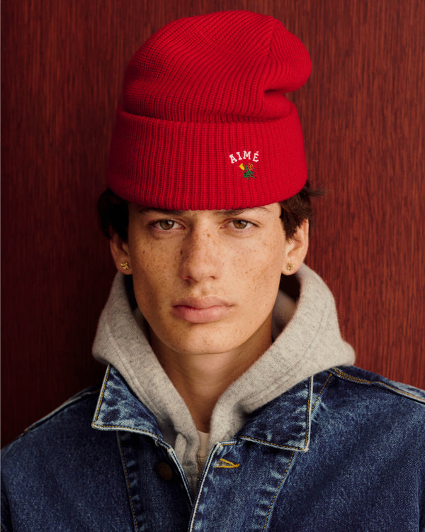 Someone in a Crest Merino Wool Beanie, gray hoodie, and denim jacket stands by a wood-textured background.