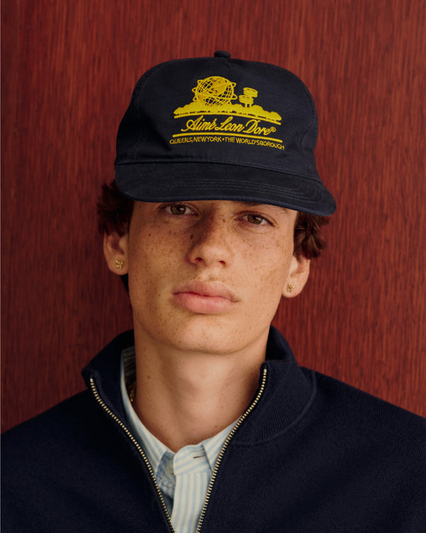 Someone sports the Unisphere Hat and a dark jacket, posed before a reddish-brown backdrop.