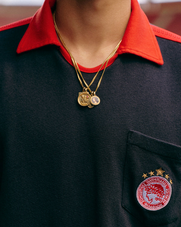 Close-up of an ALD / Olympiacos F.C. Heritage Ringer Polo with a red collar, worn with two gold pendant necklaces.