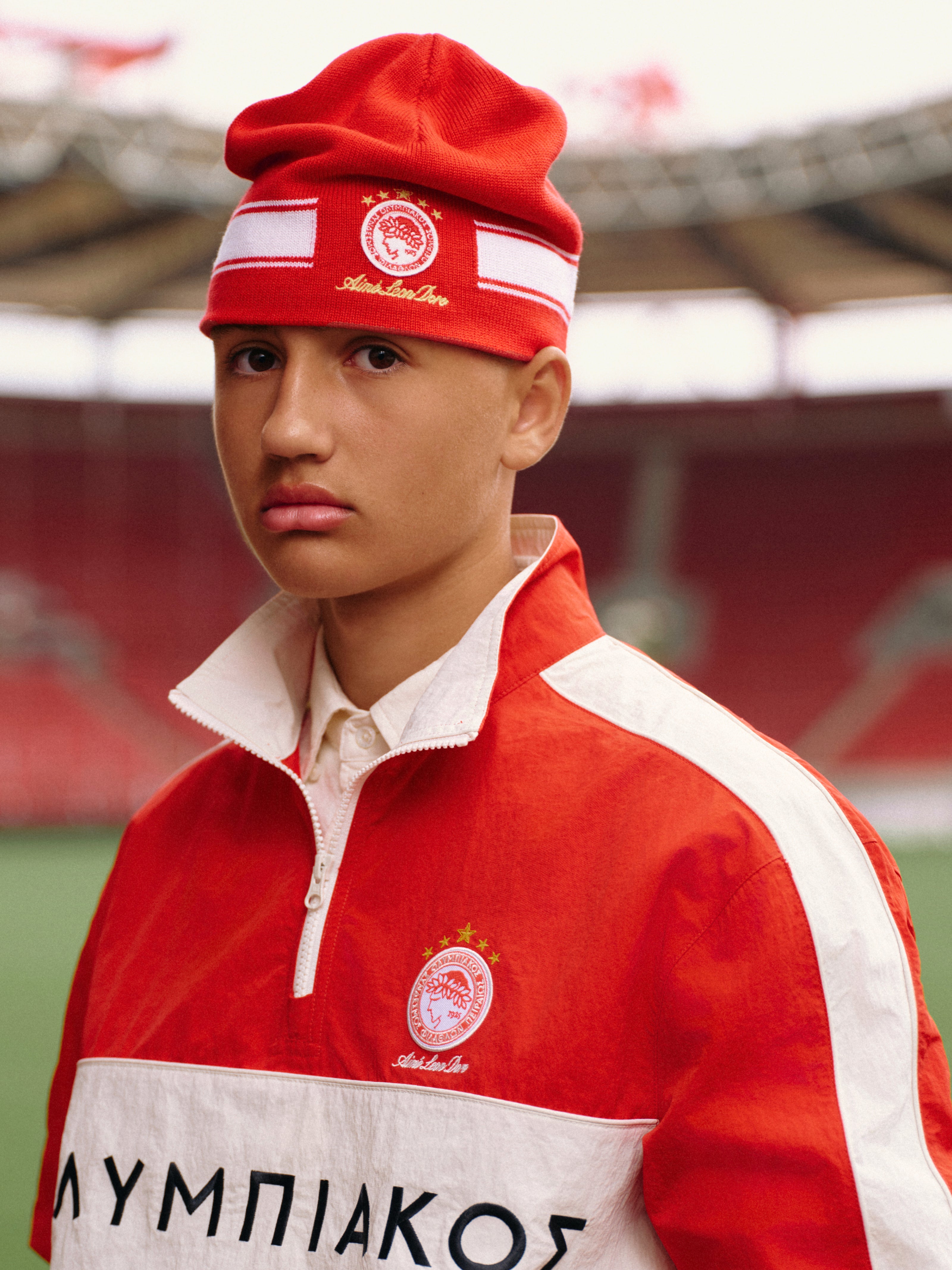 Person wearing an ALD / Olympiacos F.C. Nylon Quarter Zip Pullover and a matching beanie in a stadium.