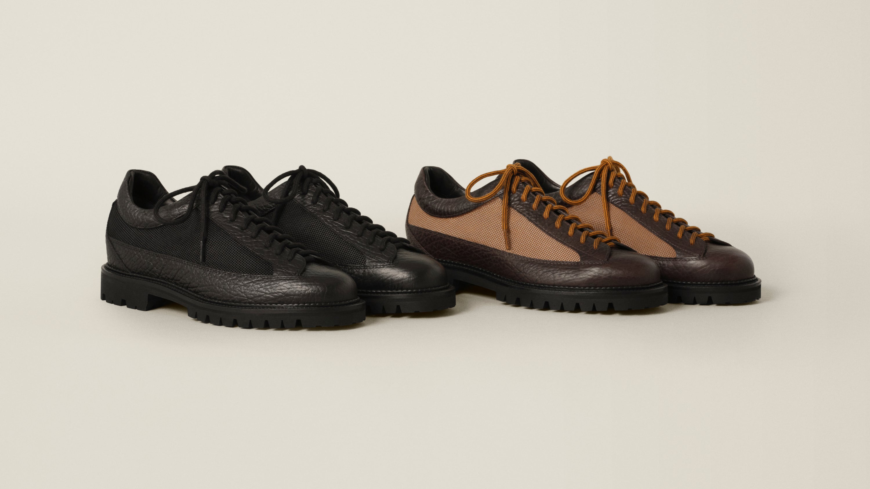 Two pairs of rugged lace-up shoes on a light beige studio background. The left pair is solid black leather with black laces and black soles.