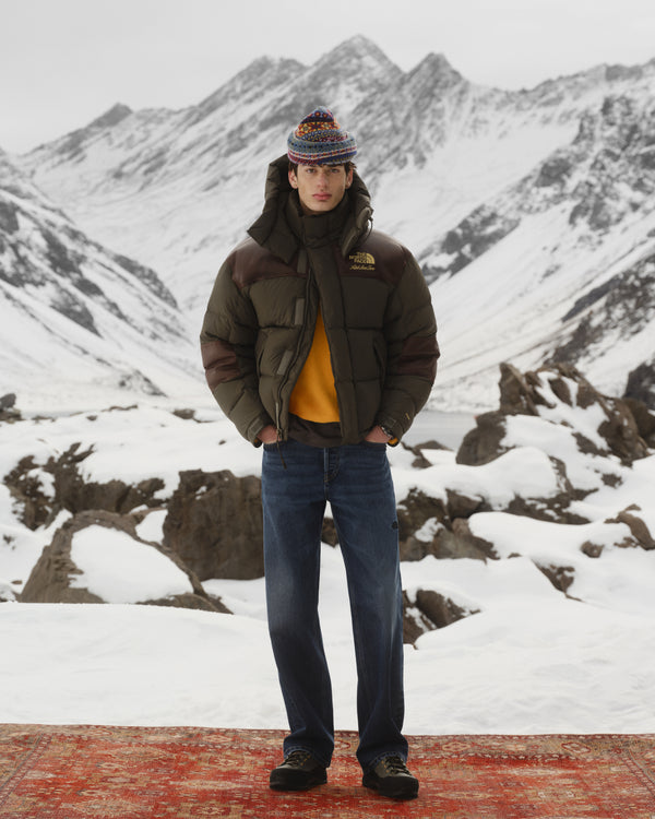 Person in ALD/The North Face Verto Alpine GORE-TEX Hiking Shoes stands on a rug amid snowy, rocky mountain peaks.