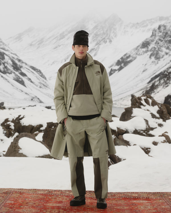 A person in layered winter clothing wears the ALD/The North Face Jacquard Beanie on a snowy mountain red carpet.
